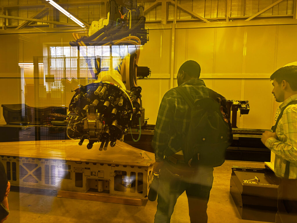 ACC tour attendees standing while looking at robotic equipment up close.